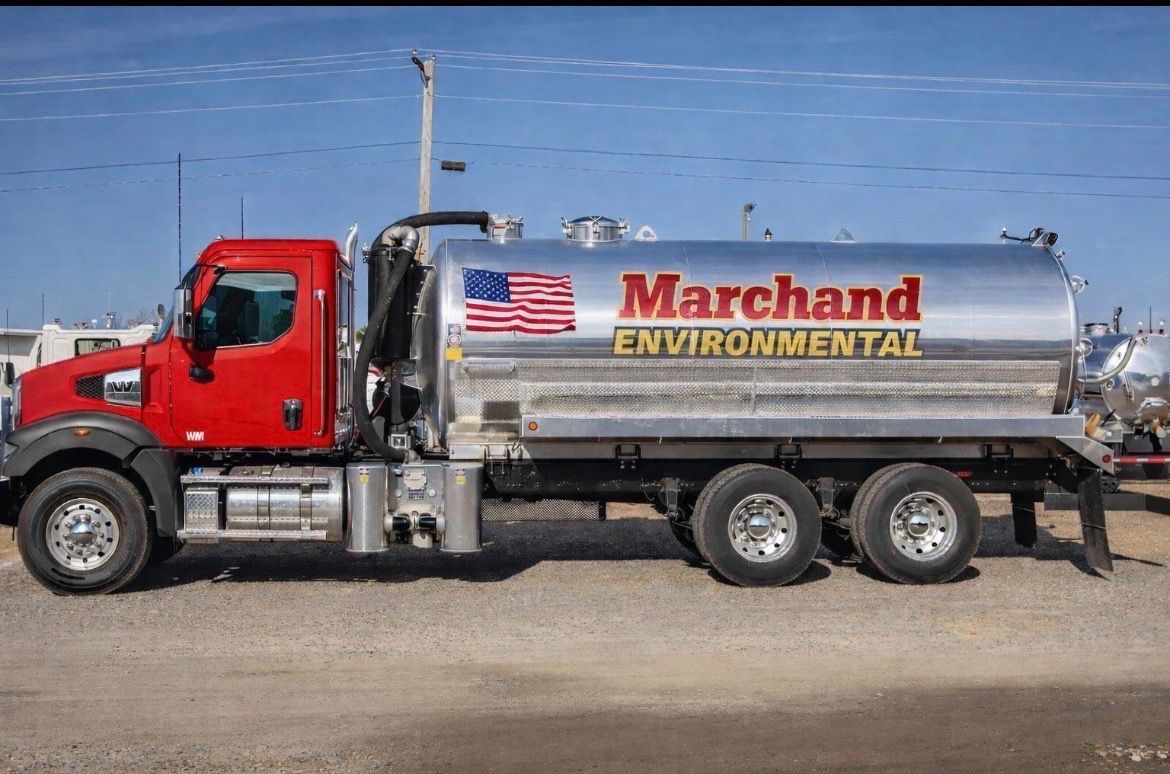 Red and silver Marchand Environmental truck with American flag on tank, parked on pavement.