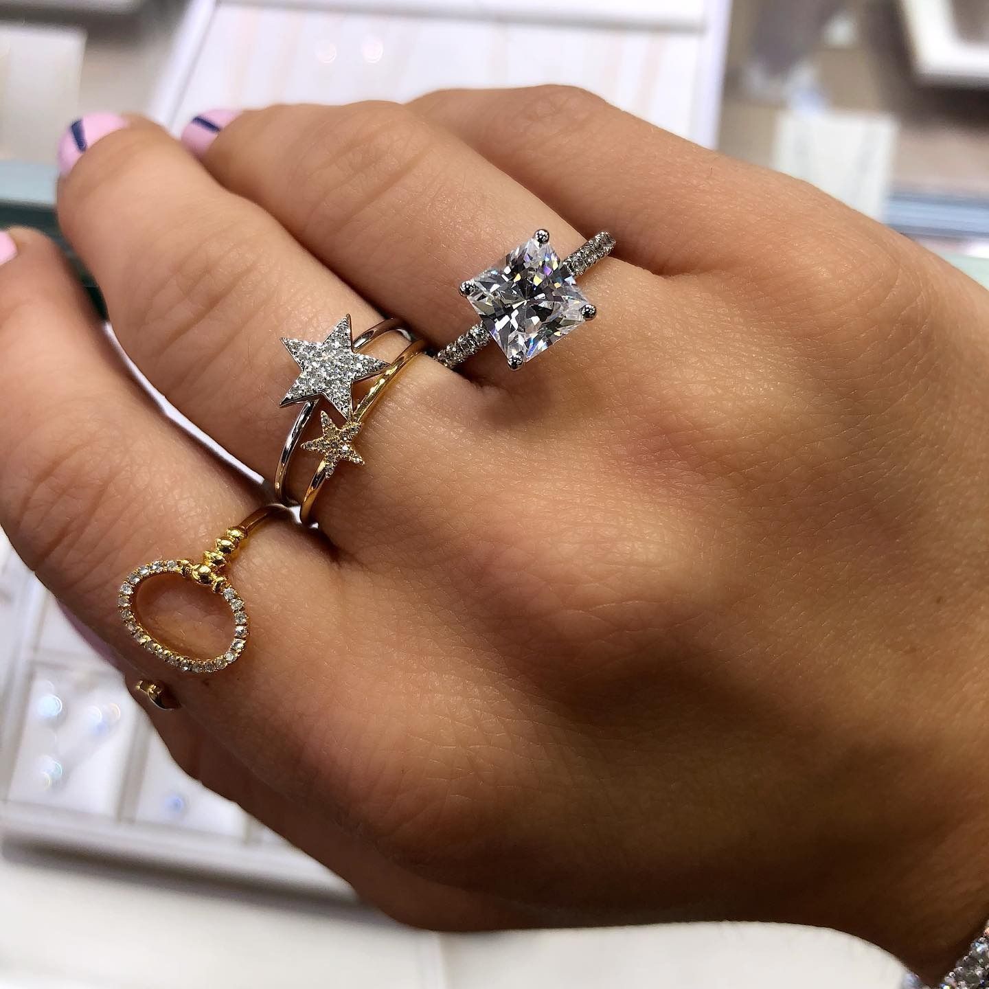 Hand wearing multiple rings, including star and heart-shaped designs with diamonds, on a light-skinned hand.