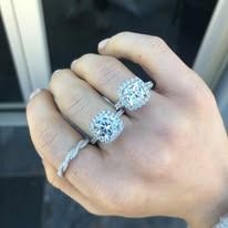 Hand with multiple rings, featuring two large diamond halo engagement rings, and a thin twisted band.