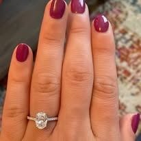 Person's hand with burgundy nails showing off an oval diamond engagement ring.