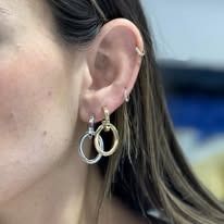A woman's ear with two hoop earrings, one silver and one gold. She has long, light brown hair.