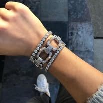 Close-up of a wrist with three diamond bracelets and a white sneaker.