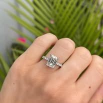 Hand wearing an emerald-cut diamond ring, set against a green plant background.