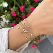 Wrist with a stack of delicate bracelets, some with small gems, in front of a blurred flower background.