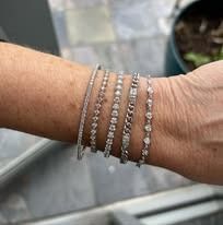 Close-up of a person's wrist wearing multiple diamond bracelets in silver tones.