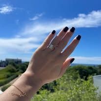 Hand with engagement ring against a blue sky.
