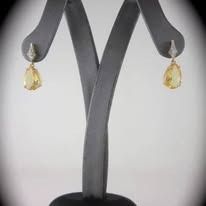 Earrings displayed on a jewelry stand. Gold teardrop-shaped gems with diamond accents.