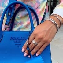 Woman holding a bright blue Prada bag, wearing rings and bracelets; tie-dye shirt.