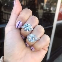 Hand displaying two diamond engagement rings, with pink and purple nail polish.