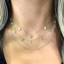 Close-up of a person's neck wearing three delicate gold necklaces with small, teardrop-shaped pendants.