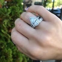Hand wearing pear-shaped diamond engagement ring with a matching band; outdoors.