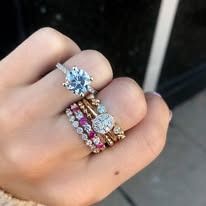 Hand wearing multiple rings, including a large blue gemstone, with other smaller diamond and ruby bands.