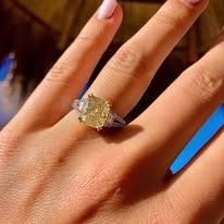 Hand wearing a gold ring with a large yellow gem, outdoors in sunlight.