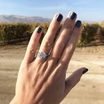 Close-up of a hand with a diamond engagement ring, outdoors. Ring is in focus.