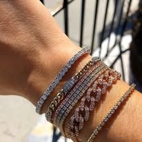 Close-up of wrist adorned with several diamond tennis bracelets and a gold chain bracelet.