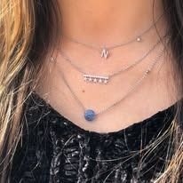 Woman wearing three layered necklaces, including a single initial 