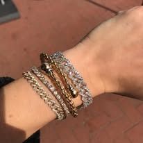 A wrist adorned with several gold and diamond bracelets, against an outdoor setting.