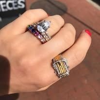 Hand wearing two ornate rings: a large white diamond ring and a rectangular gold ring.