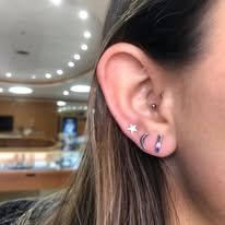 Close-up of a person's ear with multiple earrings: a star, a crescent moon, and a small stud.