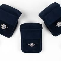 Three navy blue ring boxes each hold a diamond ring.