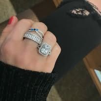 Hand wearing multiple rings, including a large square diamond and a stack of bands.