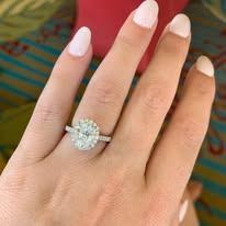 A hand wearing a diamond engagement ring, showcasing the sparkling stone, over a patterned fabric background.