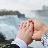 Hands clasped, wearing rings, Niagara Falls backdrop.
