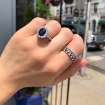 Hand wearing two diamond rings, one with a blue stone, outdoors.