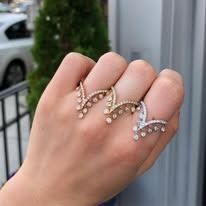 Hand wearing three diamond-studded chevron rings, gold, and white gold, outdoors.