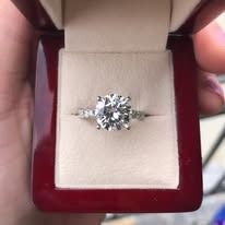 Diamond ring in a red jewelry box, held in a person's hand.