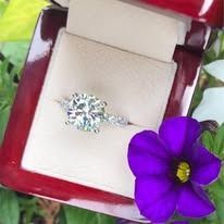 Diamond ring in a red velvet box, next to a purple flower.