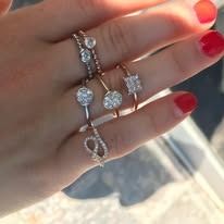 Hand wearing several diamond rings, with red nail polish.