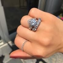 Hand wearing two rings: a large, ornate engagement ring and a smaller band.