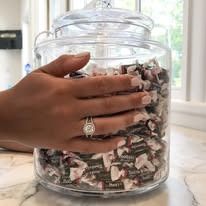 Hand with ring reaches into a clear jar filled with wrapped candies.