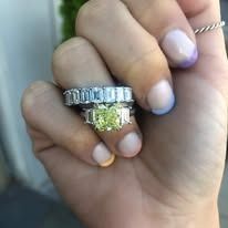 Hand wearing several diamond rings, with a colorful manicure.