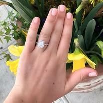 A hand with a diamond ring, rests on yellow flowers near greenery.
