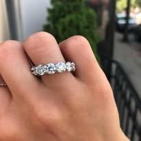 Hand wearing a diamond eternity ring, with a green bush in the background.