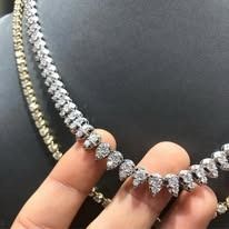 A close-up of a hand holding two diamond necklaces, one gold and one silver, against a dark background.