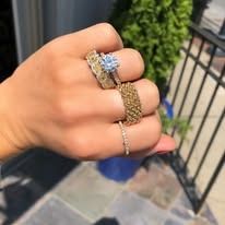 A hand displaying multiple rings. Gold and silver bands with gemstones.