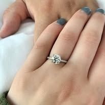 Close-up of a hand with a diamond engagement ring, resting on another hand. Gray nail polish.