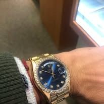 Gold Rolex watch with a blue face and diamond bezel on a wrist.