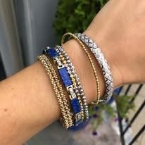Close-up of a wrist with multiple gold and gemstone bracelets, with a green plant in the background.