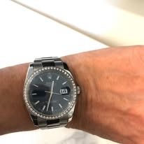 Wrist wearing a silver watch with a dark blue face and diamond-studded bezel.