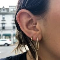 Close-up of a woman's ear with multiple gold earrings, set outside a building.