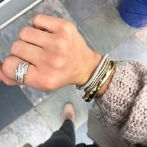 Hand wearing multiple gold bracelets and ring, sweater in the background.