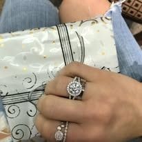 Person's hand with diamond rings, holding a decorative patterned paper with a jewelry-like design.