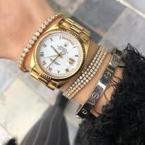 Close-up of a wrist with gold Rolex watch and diamond bracelets.
