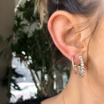 Close-up of a person's ear, wearing hoop earrings with diamonds.