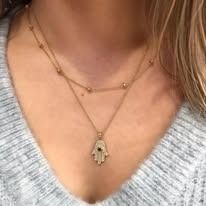 Woman wearing layered gold necklaces; one with a hamsa hand pendant.
