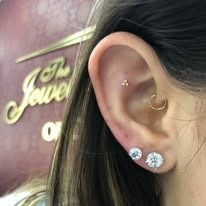 Close-up of a person's ear with multiple piercings, including a helix and lobe piercings.